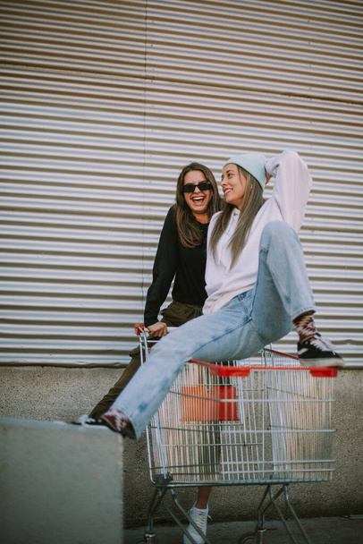 Two pretty best friends having fun while standing on the market cart - Foto, imagen