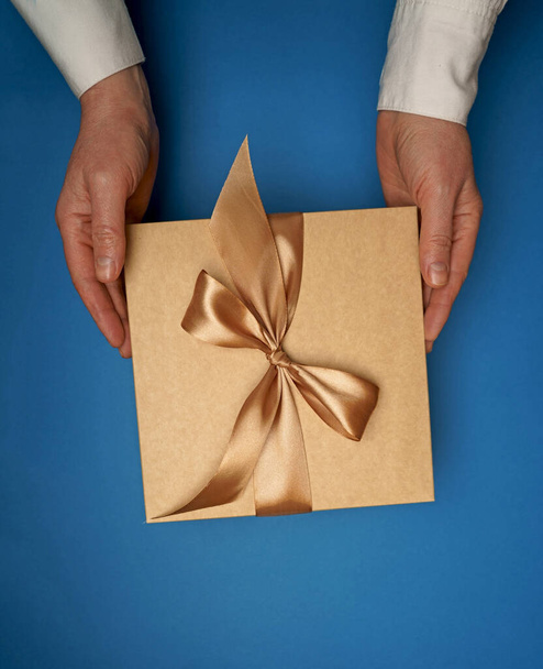 On a blue flat background hands hold a gift - Foto, Imagen