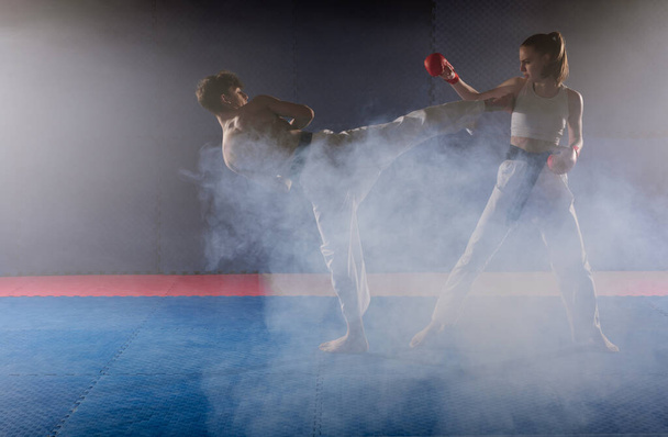 Close up of two young karate friends doing the Mawashi Geri practice in the smoke at the karate studio - Photo, Image