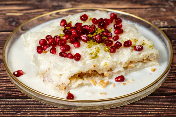 Gullac dessert. Ramadan dessert. Gullac garnished with pomegranate and pistachio in glass plate on wood background. Symbolic food. - Photo, Image