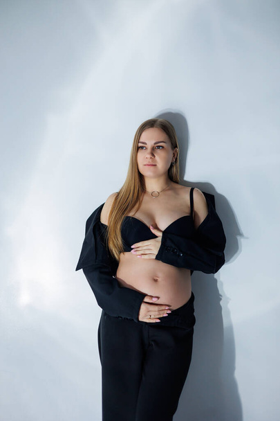 Aranyos terhes nő a stúdióban. Terhes nő fekete öltönyben. Boldog terhes nő - terhes fotó gyönyörű fiatal várandós anya szürke háttér, stúdió fotó - Fotó, kép