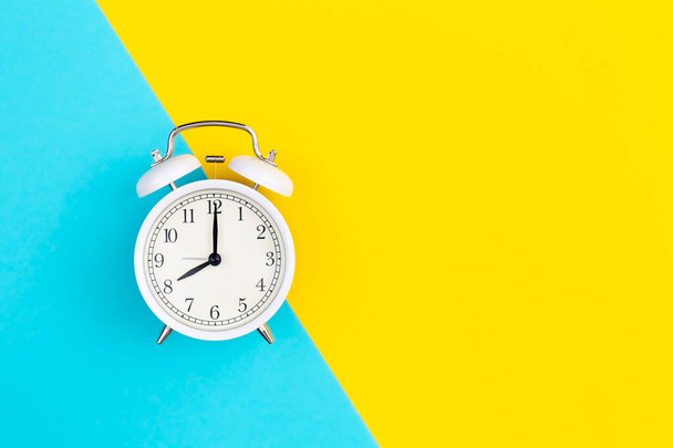 White alarm clock on a blue and yellow background, flat lay, copy space. - Foto, afbeelding