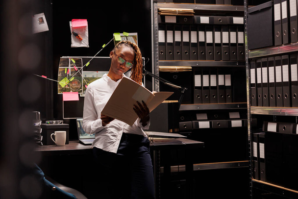Naispoliisi lukee rikosrekisteriä virassa. Afrikkalainen amerikkalainen yksityisetsivä silmälasien sisällä, jolla on rikostekninen asiantuntemus kansio ja joka tutkii päätelmiä - Valokuva, kuva