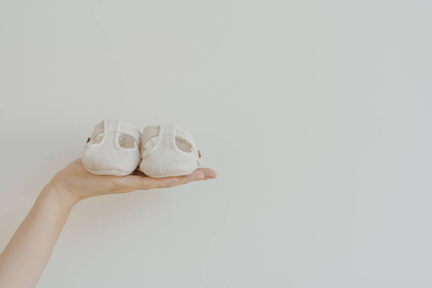 Person's hand hold cute little baby sandals shoes on white background. Minimalist baby fashion apparel - Foto, imagen