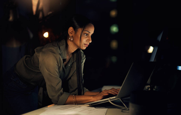 Sie behält die Frist im Auge. eine junge Geschäftsfrau, die nachts in einem Büro an einem Laptop arbeitet - Foto, Bild