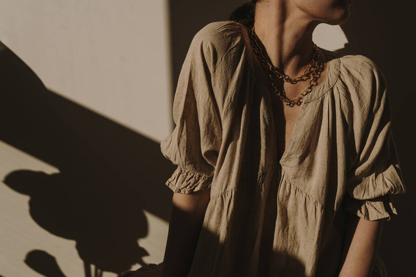 Nuori kaunis nainen neutraali beige pellava sundress, pukeutua auringon valo varjot. Tyylikäs ylellinen boheemi esteettinen elämäntapa trendikäs tyylikäs koostumus. Muoti vaatteita auringonvalo varjo heijastuksia - Valokuva, kuva