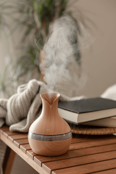 Aroma oil diffuser lamp on blurred background with books and knitted element. - Photo, Image