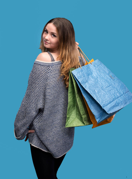 Όμορφο κορίτσι με τσάντες για ψώνια ποζάρει σε μπλε φόντο - Φωτογραφία, εικόνα