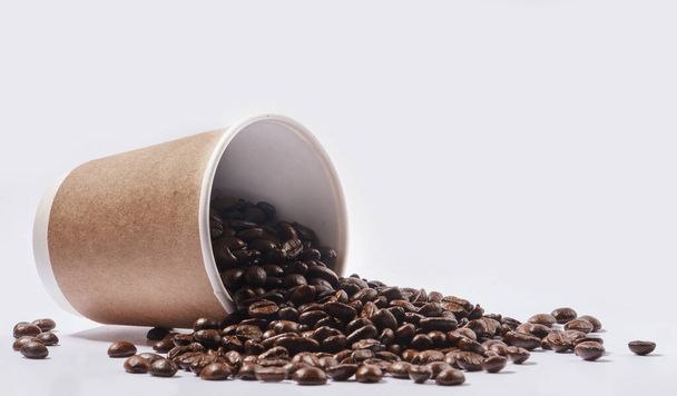 Bringing energy to your mornings. Studio shot of a tipped over paper cup filled with coffee beans against a white background - Photo, Image