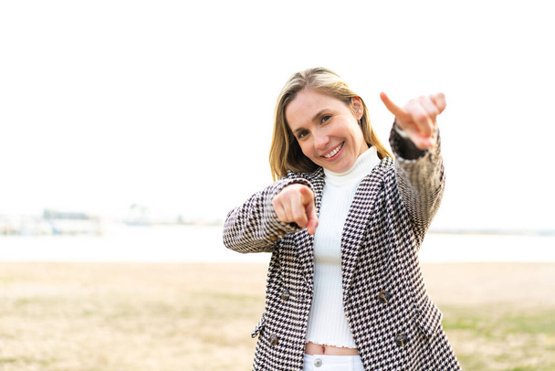 Junge blonde Frau im Freien zeigt lächelnd mit dem Finger auf dich - Foto, Bild