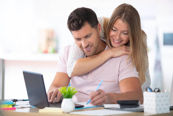 positive young couple embracing and calculating the bills at home - Foto, imagen