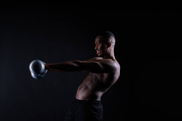vertrouwen jonge man shirtless portret training met stom-bell tegen zwarte achtergrond. - Foto, afbeelding