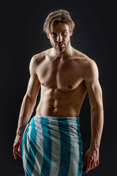 muscular man with towel on torso isolated on black background. man with muscular torso in studio. muscular man wearing towel on torso. photo of man having muscular torso. - Zdjęcie, obraz