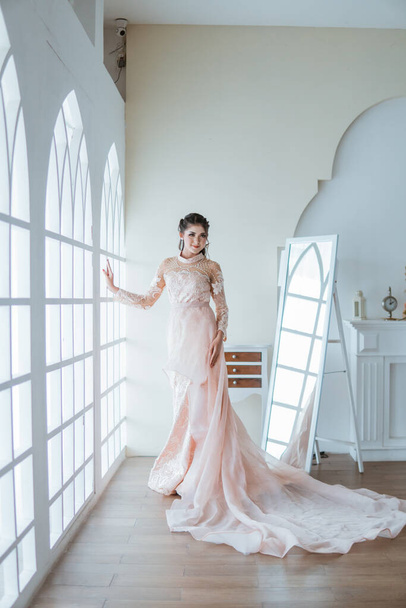 asian bride in orange long tail gown standing between the window and the mirror - Fotoğraf, Görsel