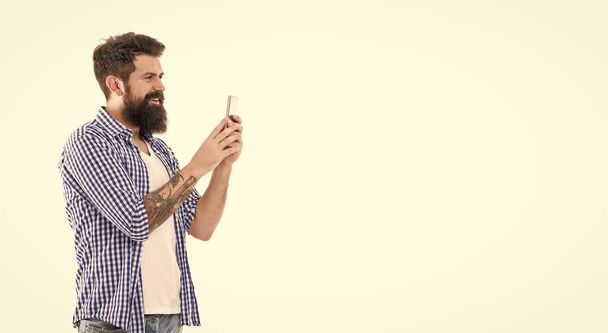 smiling brutal bearded man taking photo with phone isolated on white background with copy space. - Фото, зображення