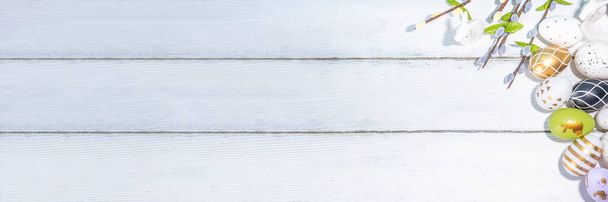  Άνοιξη Πάσχα διακοπές φόντο ευχετήρια κάρτα. Ιτιά άνοιξη κλαδιά λουλουδιών, πολύχρωμα πράσινα, χρυσά αυγά του Πάσχα στο καλάθι, με ετικέτα Καλό Πάσχα σε λευκό ξύλινο φόντο top view copy space - Φωτογραφία, εικόνα