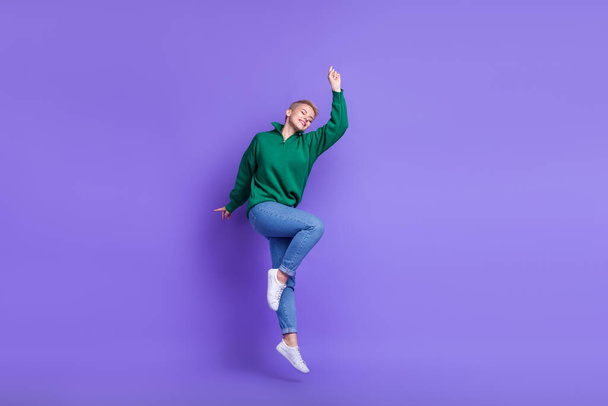 Full length photo of sweet adorable woman dressed green pullover jumping high isolated purple color background. - Foto, Imagen