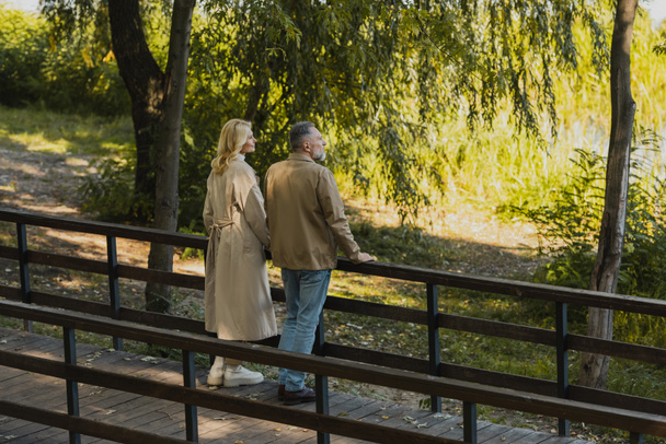 Side view of middle aged couple looking away while standing on bridge in spring park  - Foto, Bild