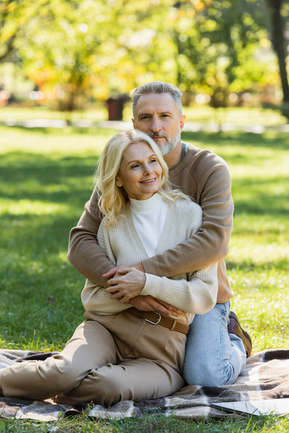 hombre de mediana edad con barba gris abrazando encantadora esposa rubia en el parque verde  - Foto, imagen