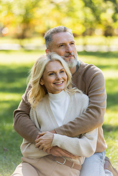 happy middle aged man with grey beard hugging charming wife in green park  - Φωτογραφία, εικόνα