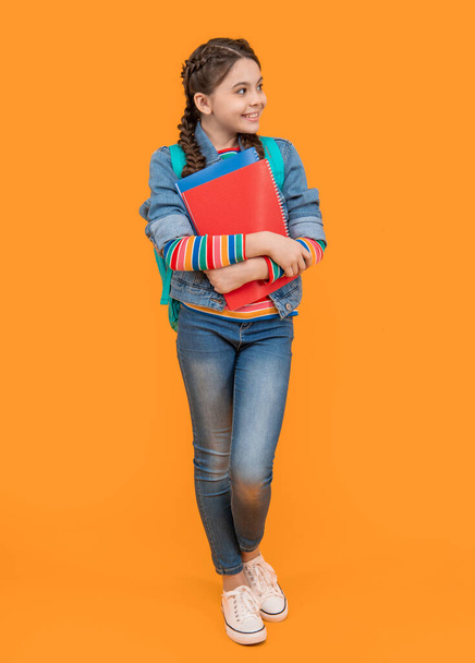 Szczęśliwy nastolatek z powrotem do szkoły. Nastolatka trzymająca książki. Nastolatek uśmiechnięty patrząc na żółte tło. Dzień wiedzy. 1 września. - Zdjęcie, obraz