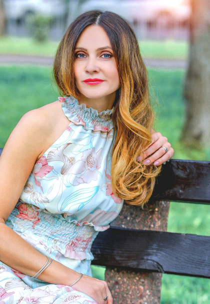  ortrait fille blanche assise sur un banc dans le parc. Robe d'été légère, imprimé floral. Paysage urbain. Mode - Photo, image
