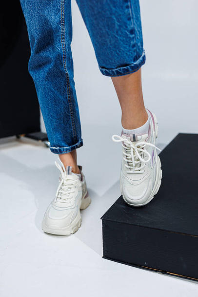 Casual women's fashion. Sports shoes for women. Slender female legs in jeans and white stylish casual sneakers. Women's comfortable summer shoes. - Foto, afbeelding