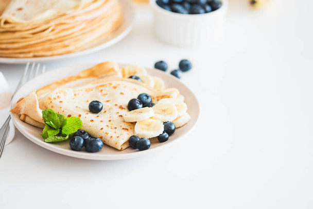 French crepes with banana and blueberries on white table. Copy space - Фото, зображення
