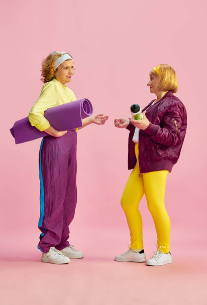 Friends meeting. Elderly sportive woman in colorful uniform posing with fitness equipment against pink studio background. Concept of sportive lifestyle, retirement, health care, wellness. Ad - Foto, afbeelding