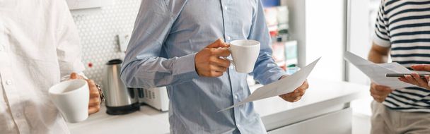 Group of diverse coworkers drink coffee during break and talking about work. Blurred background - Photo, image