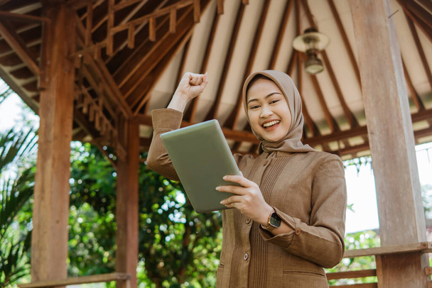 female teacher in hijab smiling while using a tablet with gazebo in the background - Foto, Imagen