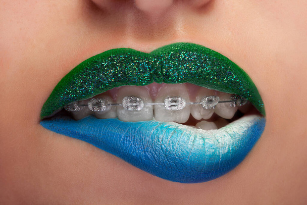 Close up mouth blue and green lips with glitter brackets. Fashion make up. Make up addiction. Artistic make up. Macro shooting. Sensuality and fashion concept - Photo, Image