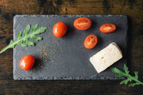 Třešňová rajčata se sýrem a rukolou na černém přírodním stánku v detailní scéně. Kvalitní fotografie - Fotografie, Obrázek