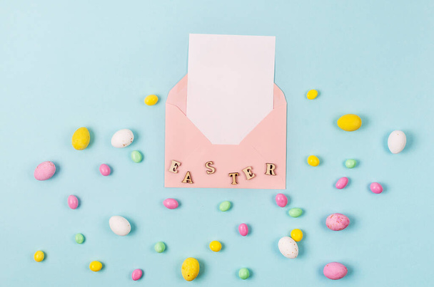 Colorful candy easter eggs on blue background and pink envelope with blank card with place for text. Easter holiday and tradition concept.  - Photo, Image