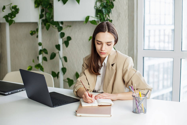 Freelancer psaní na notepad na stole v moderní zelené kanceláři. Pojetí podnikání, studia, práce a vydělávání peněz. - Fotografie, Obrázek