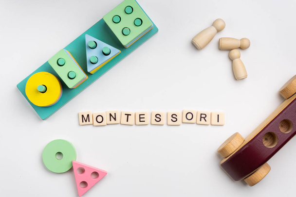Flaches Montessori-Spielzeug auf weißem Hintergrund. Wort MONTESSORI aus Kachelbuchstaben in der Mitte. - Foto, Bild