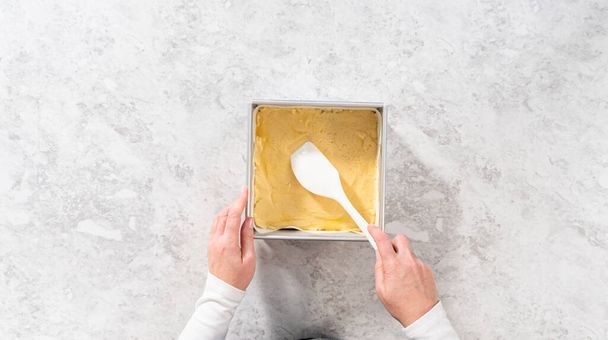 Pose plate. Remplissage carré moule à gâteau au fromage doublé de papier parchemin avec mélange de caramel pour préparer le caramel à la canne à sucre. - Photo, image