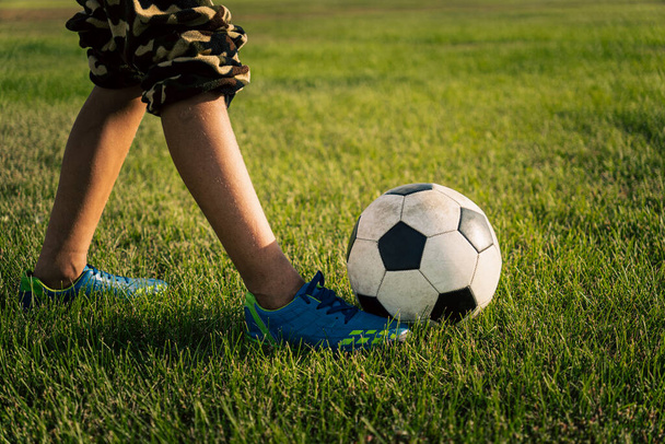 classical black and white football ball and legs of a footballer on the green grass of the field. Soccer game, training, hobby concept. with copy space. a teenage child kicks a ball. - Photo, Image