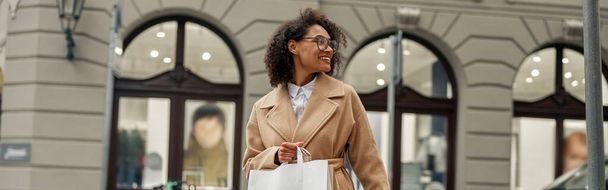 Kağıt torbalarla alışveriş yapan Afro-Amerikan kadın şehirde karşıdan karşıya geçiyor. Satış konsepti - Fotoğraf, Görsel