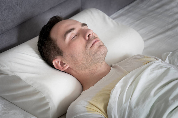 Χαριτωμένος νεαρός άνδρας κοιμάται στο κρεβάτι σε ορθοπεδικό μαξιλάρι - Φωτογραφία, εικόνα