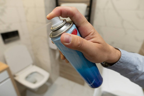 A férfi légfrissítőt permetez a fürdőszobában. WC spray egy férfi kezében a háttérben a WC-csésze. - Fotó, kép