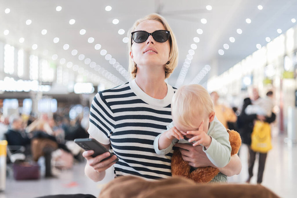 Мати подорожує з дитиною, тримає маленького хлопчика в терміналі аеропорту, перевіряє розклад польоту, чекає на посадку на літак. концепція подорожей з дітьми
 - Фото, зображення