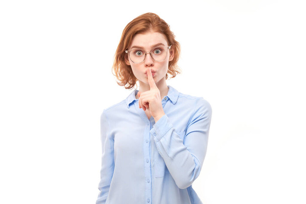 Portrait of young redhead woman covering mouth with finger isolated on white background. Asks for silence, keep secret, shh gesture - Fotó, kép
