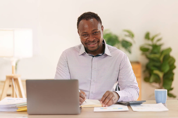 Smiling American African hace un informe financiero y estudia las cifras anuales, analiza las ganancias. Control contable de la situación financiera. - Foto, Imagen
