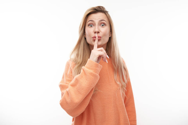 Portrait of young blond woman covering mouth with finger isolated on white background. Asks for silence, keep secret, shh gesture - Foto, Imagen