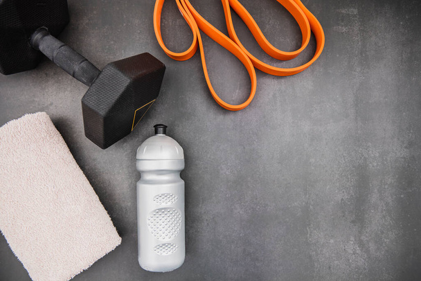 Home workout, flat lay, dark background. .Dumbbell, towel, drink, fitness rubber - Фото, зображення