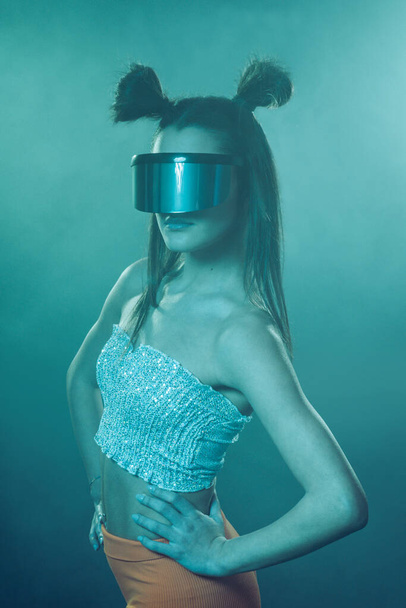 Portrait of beautiful cyber model woman posing wearing futuristic glasses on head with neon light in a virtual tech environment - Фото, изображение