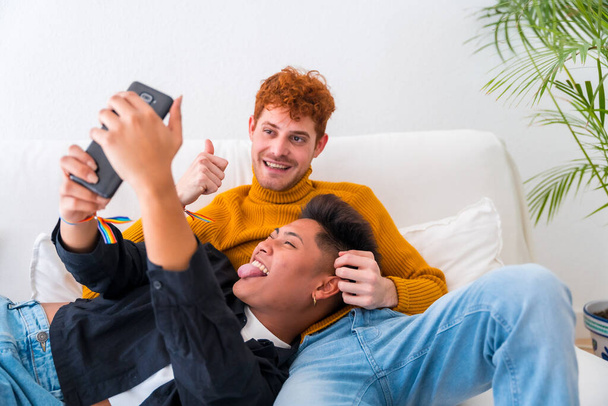 Beautiful gay couple being romantic indoors on the sofa, gay couple, taking a selfie - Fotó, kép
