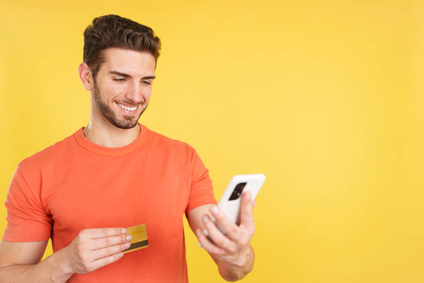Caucasian man using the mobile and card to shopping online in studio with yellow background - Foto, immagini