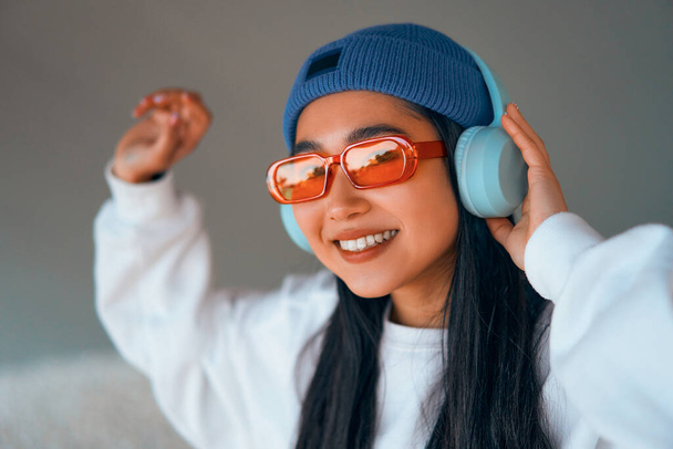 Elegante mujer joven asiática en un sombrero escuchando música en los auriculares en la calle. - Foto, Imagen